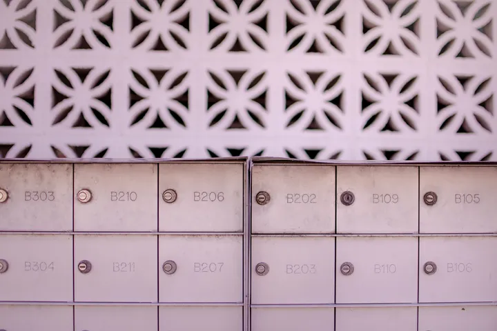 Two banks of numbered metal mailboxes set against a patterned white breeze-block wall.
