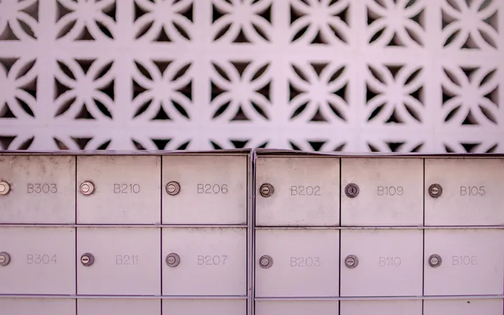 Two banks of numbered metal mailboxes set against a patterned white breeze-block wall.